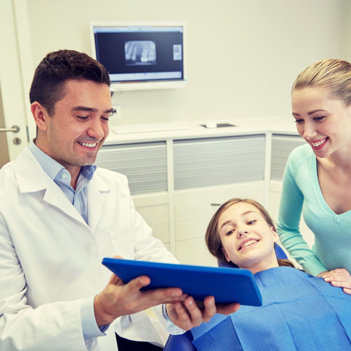 Dentist holding tablet showing dental braces photos to patient and parent using OrthoPhoto App